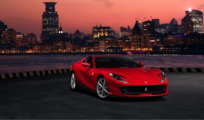 A sleek red Ferrari 812 Superfast parked in front of a cityscape at sunset.