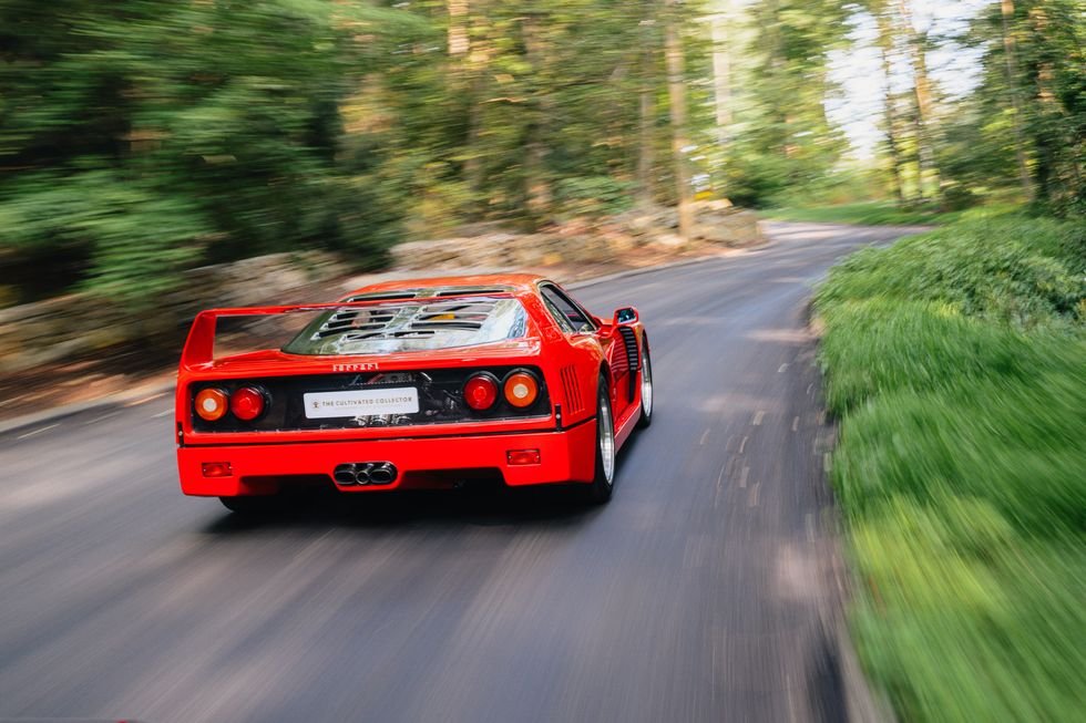 A classic red Ferrari F40 speeding down a scenic road.