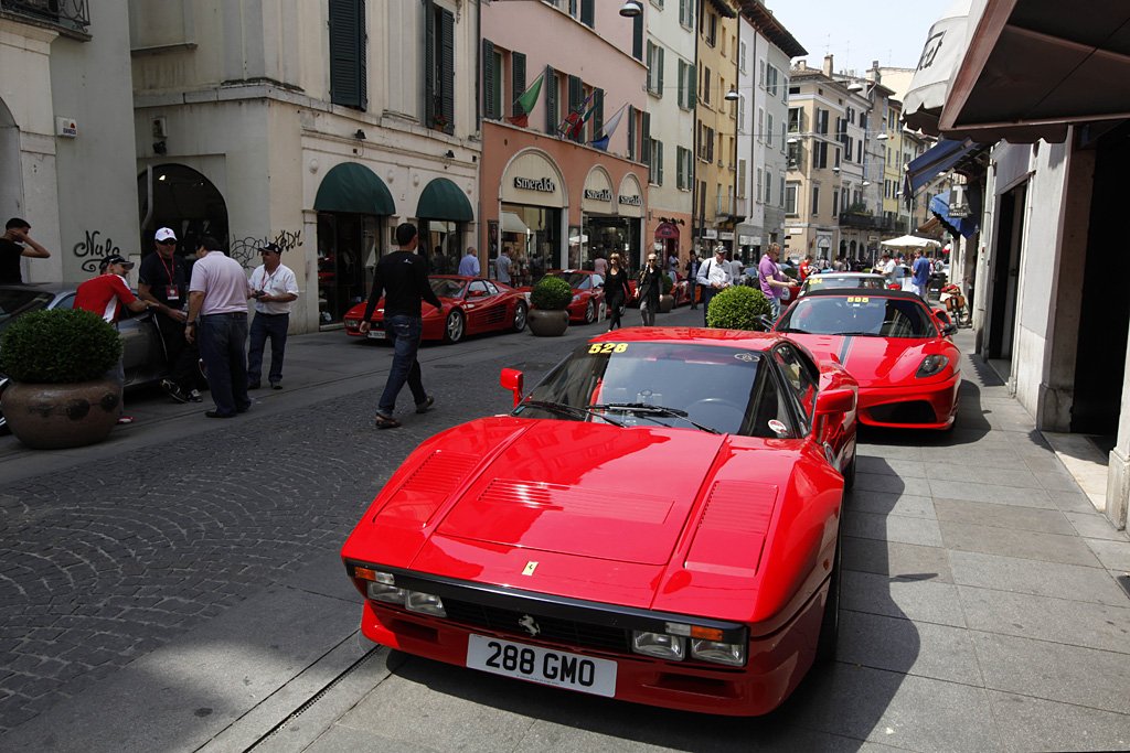 image of crown around classic red Ferraris, including a 288 GTO, parked on a cobblestone street.