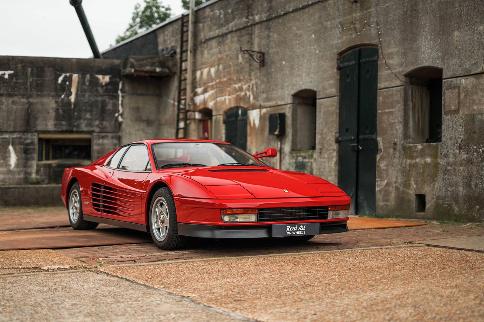 A classic red Ferrari Testarossa parked in front of a historic building.