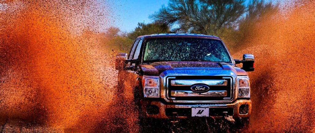 Ford Super Duty truck kicking up dramatic orange mud spray while off-roading