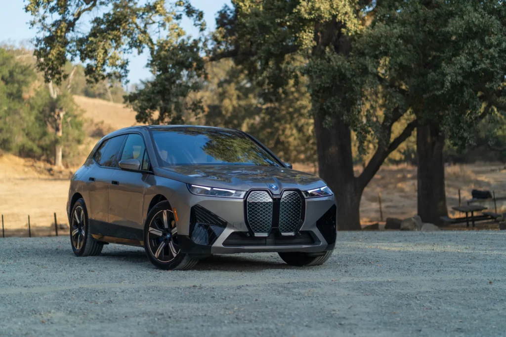 A gray BMW iX electric SUV parked on a dirt road with trees in the background