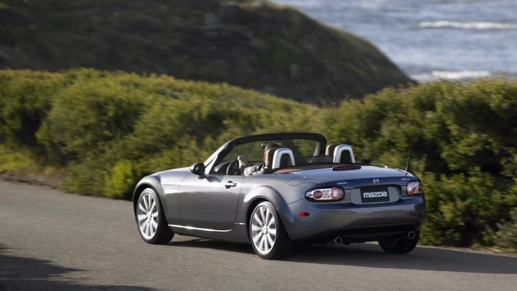 A 2008 Mazda MX-5 Miata convertible cruising along a coastal road.