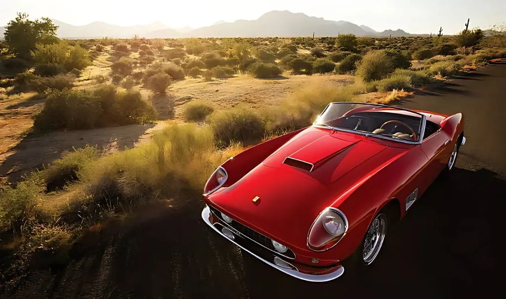 Red vintage Ferrari convertible car parked on a desert road at sunset.