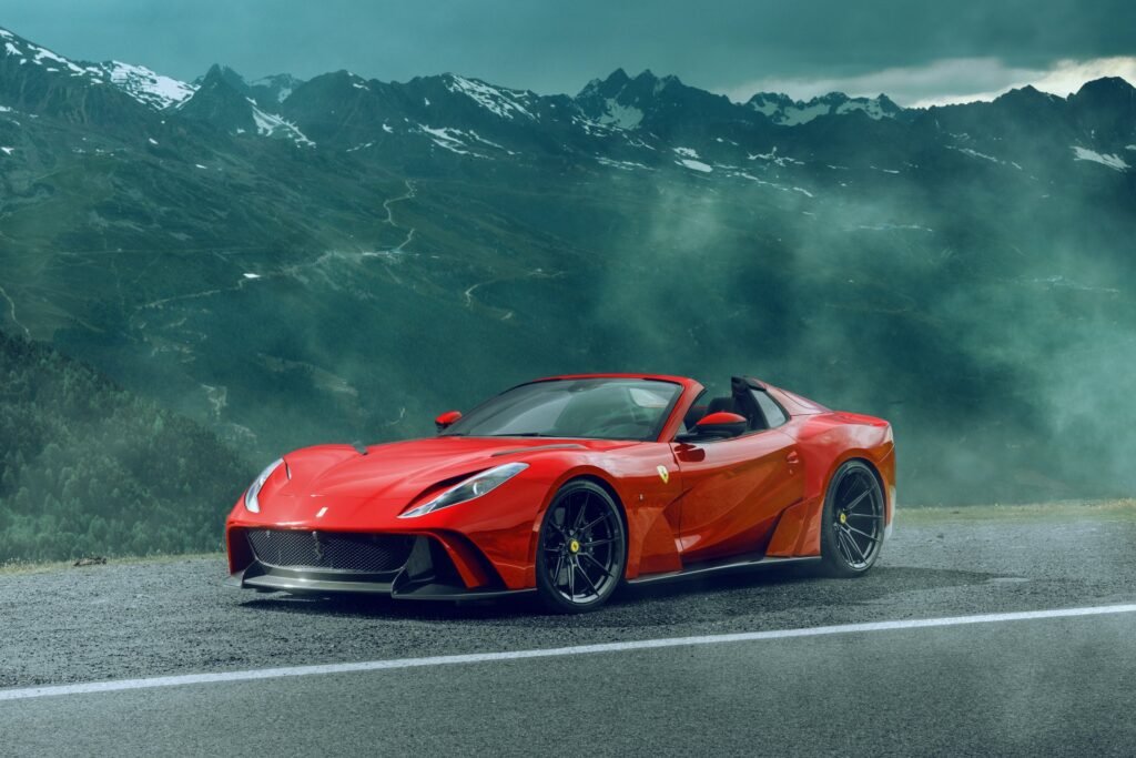 Red Ferrari 812 GTS on mountain road with misty alpine backdrop.