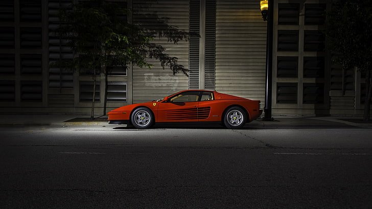 A red vintage sports car parked on the side of a street at dusk.