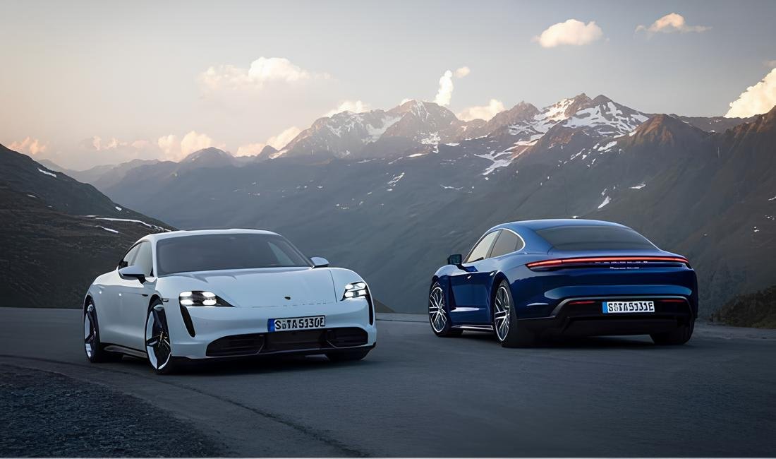 Two Porsche Taycan electric cars parked on a mountain road with a scenic backdrop.