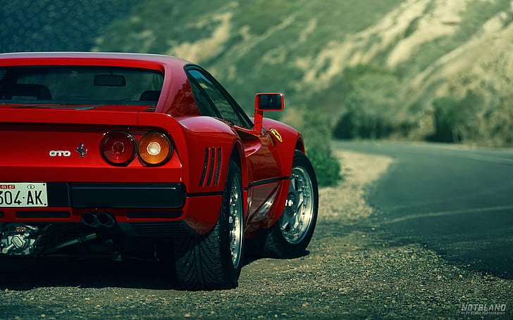 Ferrari 288 GTO parked on a roadside with a blurred greenery and hillside background.