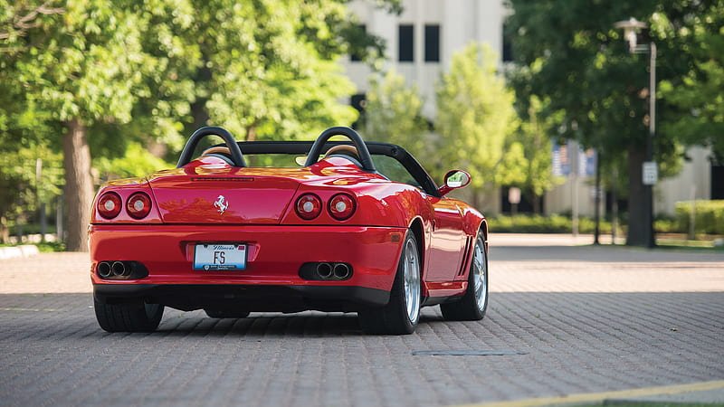 Red Ferrari convertible parked on a tree-lined street.