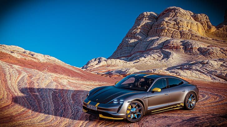 A black all electric porsche parked on a desert road with rock formations in the background