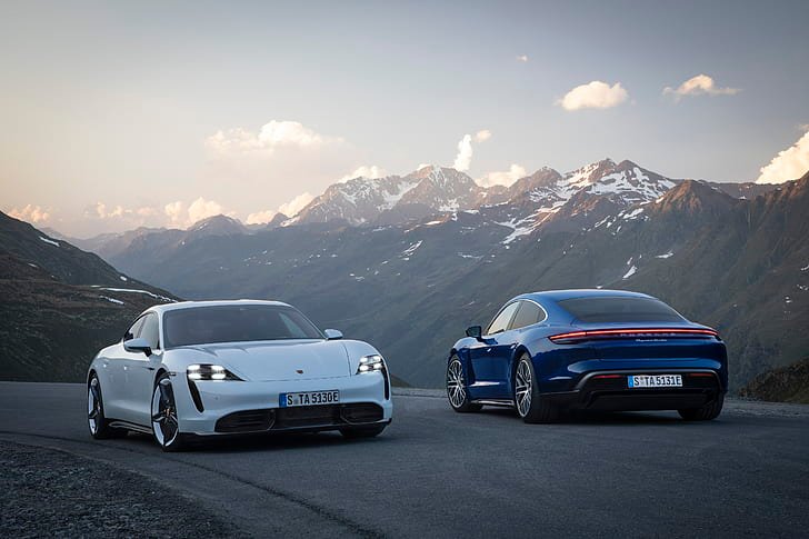 Two Porsche Taycan electric cars, side by side, are parked on a mountain road at dusk 