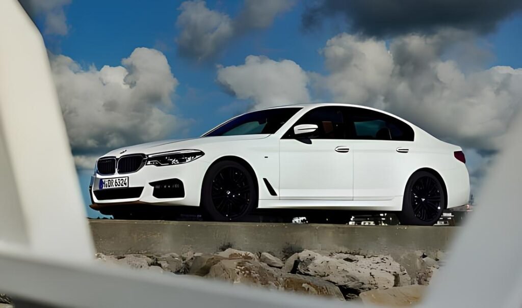 White 2016 BMW 5 Series sedan with black wheels against a cloudy blue sky