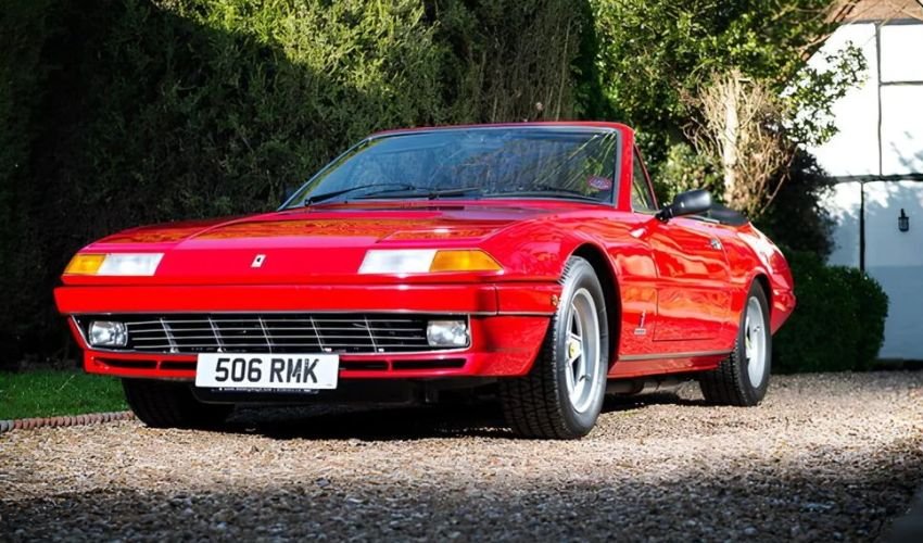 A red Ferrari 400i parked on a gravel driveway